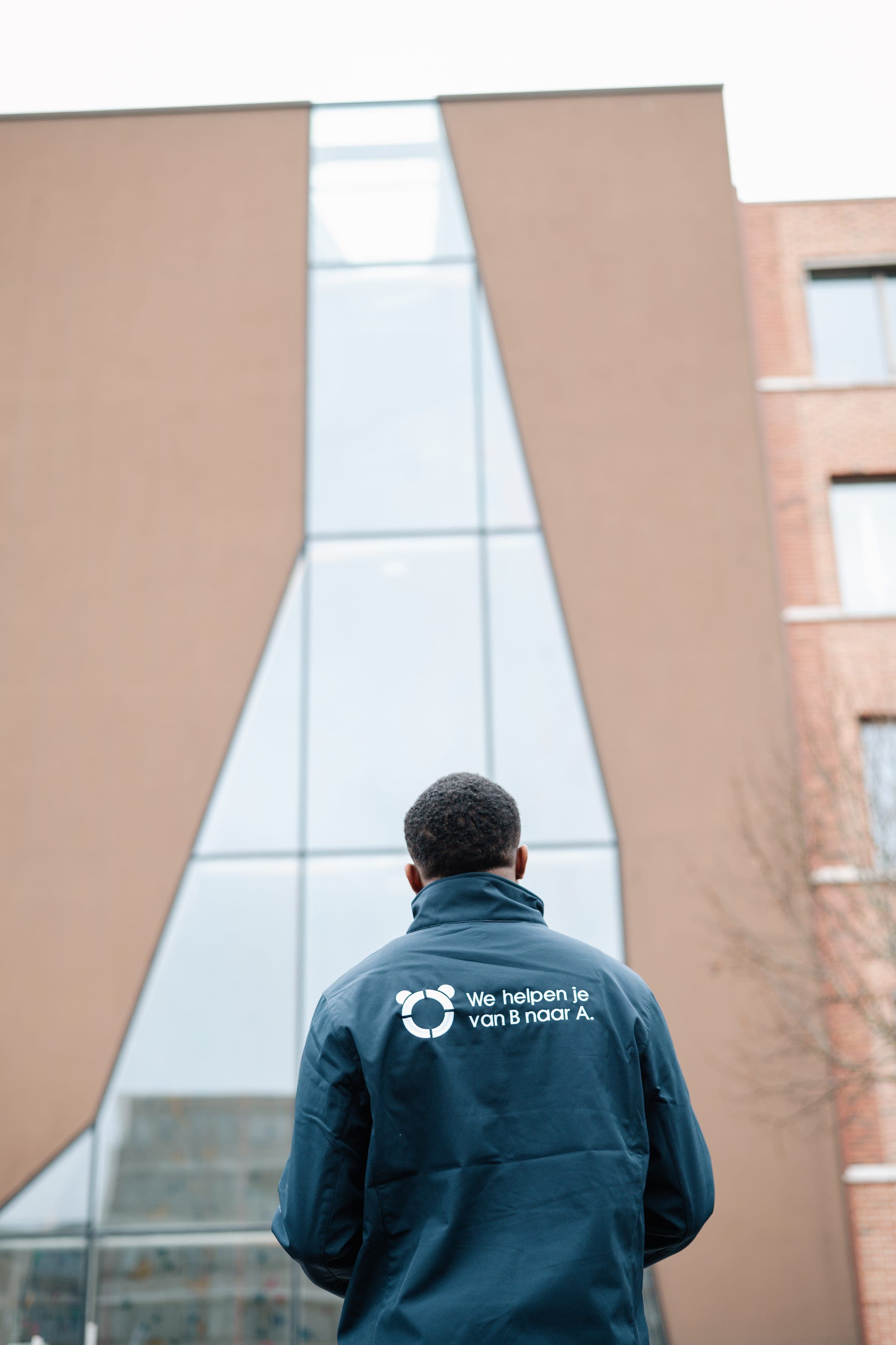 Panda-adviseur kijkt omhoog naar een markant A-vormig glazen kantoorgebouw — typisch portefeuille-asset waar label-C-handhaving en MEPS 2030 op landen